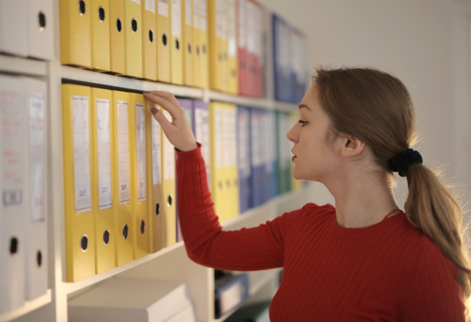 Persona eligiendo una carpeta de documentos en una estantería