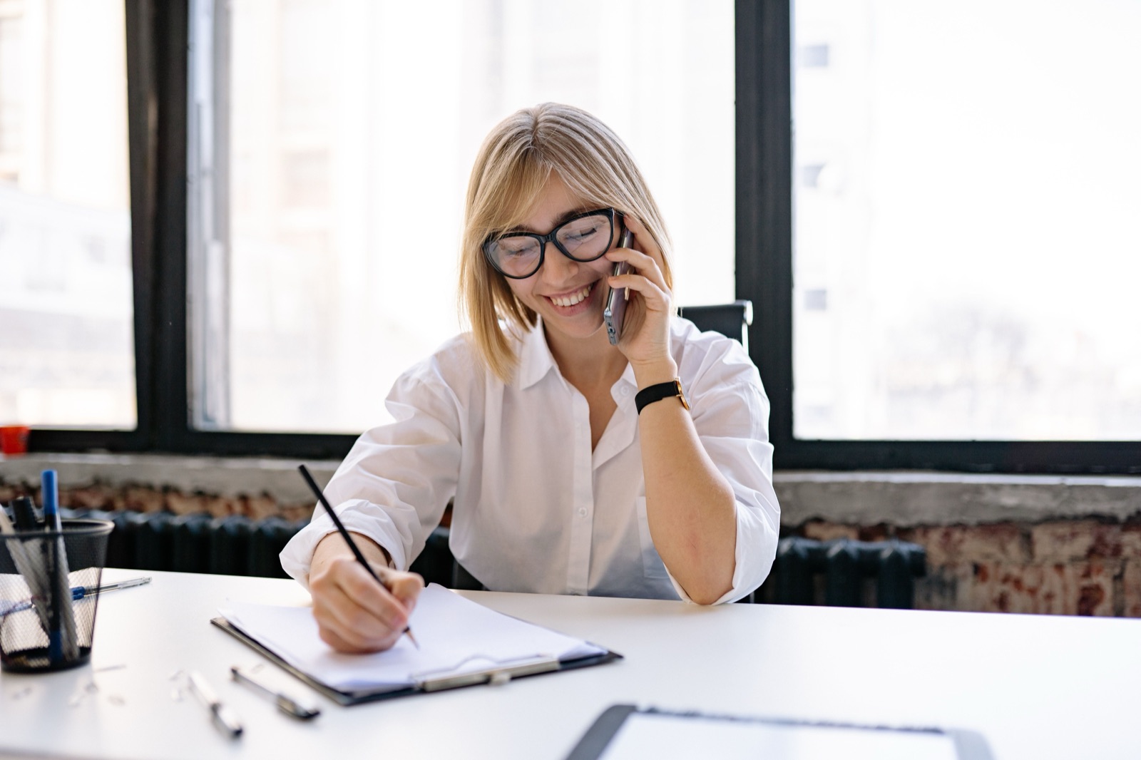 Woman smiling on a phone call while taking notes at her desk