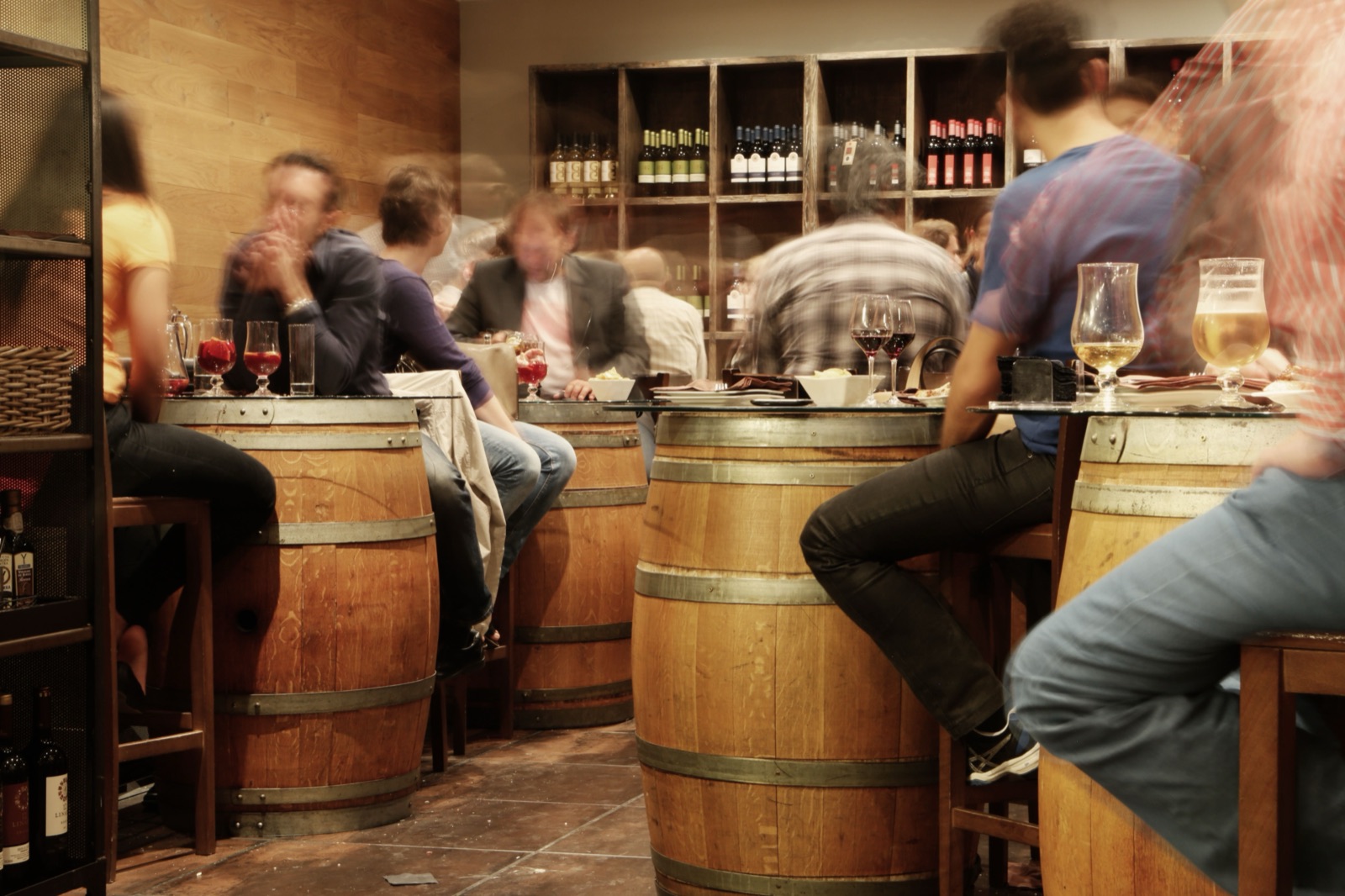 People gathered at a lively bar, seated around wine barrel tables